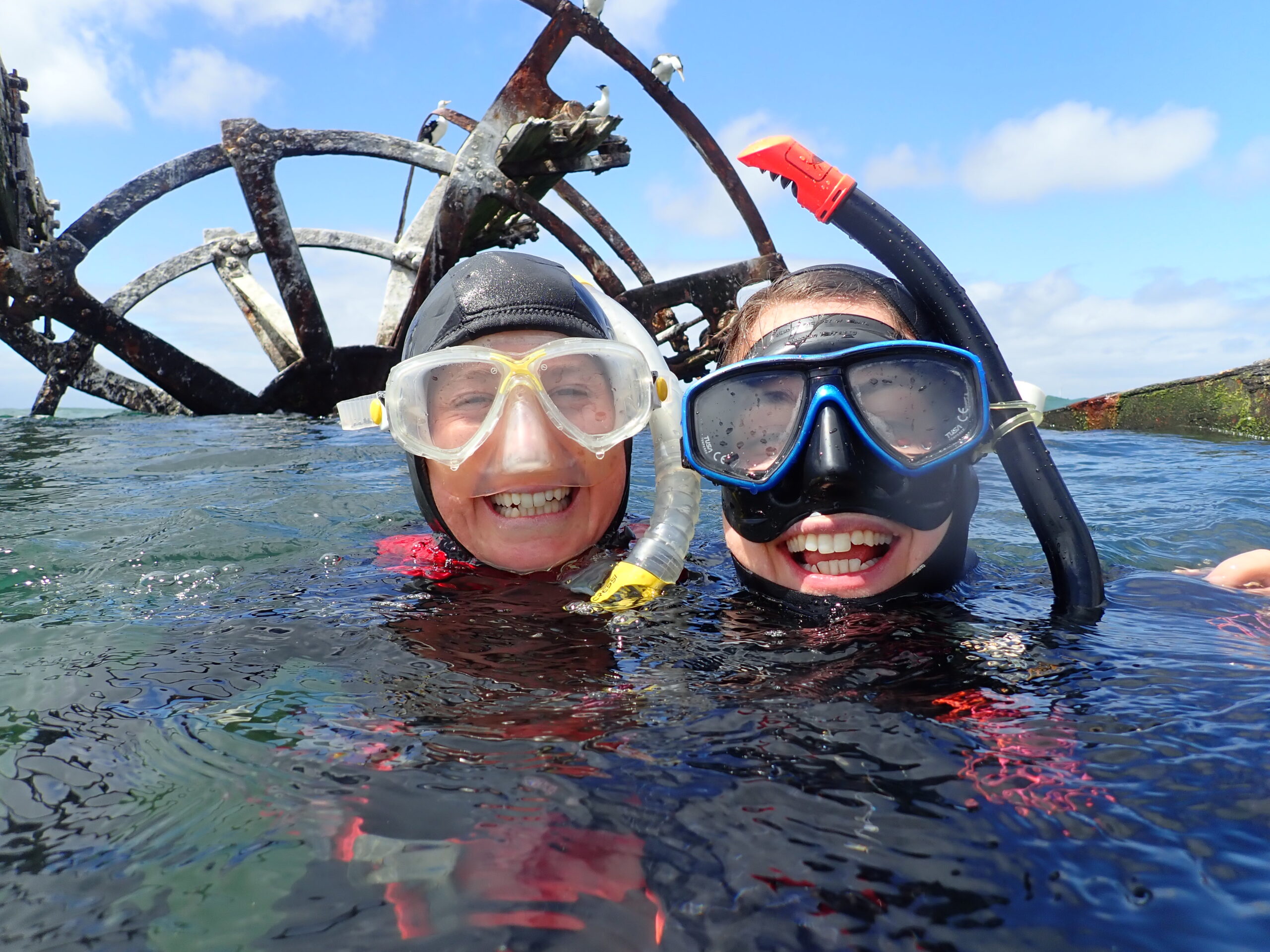 Two people in the sea wearing snorkelling masks and equipment smiling